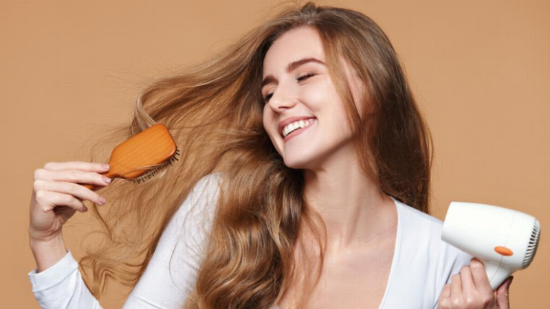 Hình ảnh một người đang sấy tóc nhẹ nhàng bằng máy sấy sau khi hấp dầu, tóc trông mềm mượt hơn
